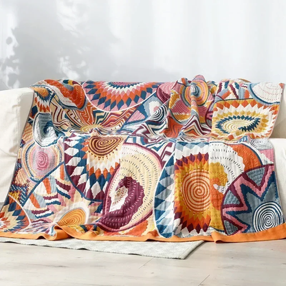 Sunburst cotton blanket draped over a white sofa, the orange border resting on a pale rug
