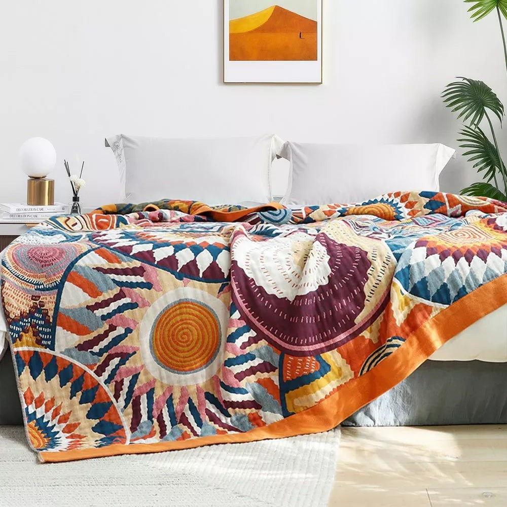 Sunburst blanket over a bed seen front on, a large orange sun and burgundy shell with the orange border down the side