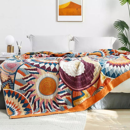 Sunburst blanket over a bed seen front on, a large orange sun and burgundy shell with the orange border down the side