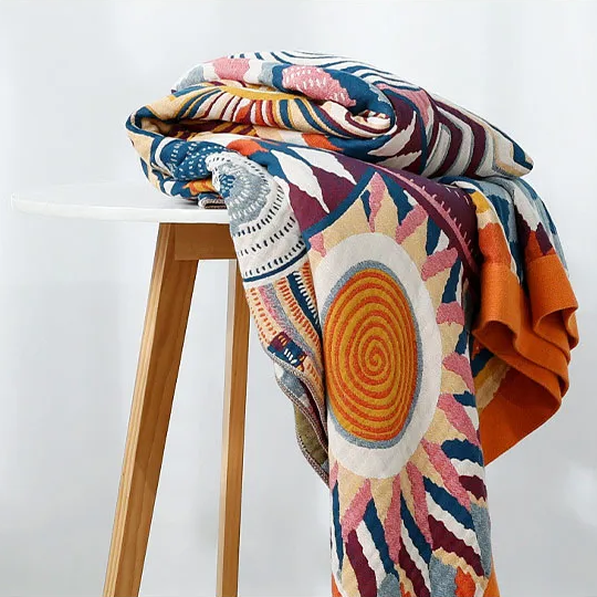 Sunburst cotton blanket folded over a white-topped wooden stool, an orange spiral sun hanging down the front