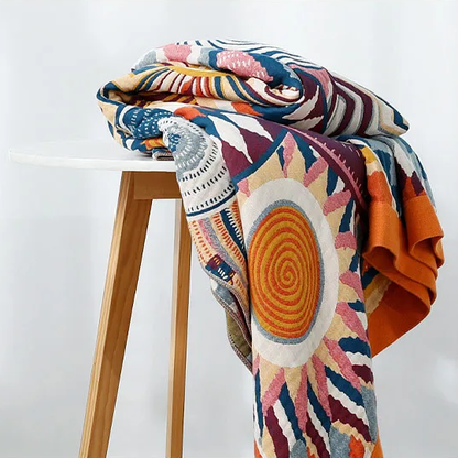Sunburst cotton blanket folded over a white-topped wooden stool, an orange spiral sun hanging down the front