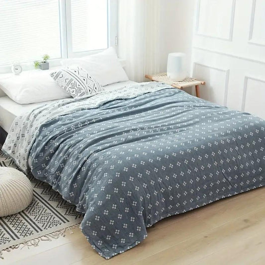 Blue diamond dot cotton blanket spread over a bed, white diamonds on slate blue with the cream reverse at one corner