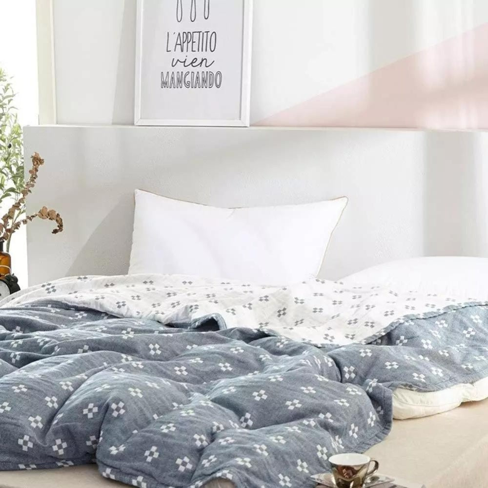 Blue cotton gauze blanket rumpled across a low bed with its cream reverse folded back at the pillows