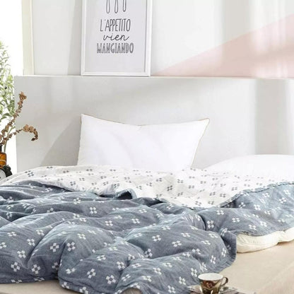 Blue cotton gauze blanket rumpled across a low bed with its cream reverse folded back at the pillows