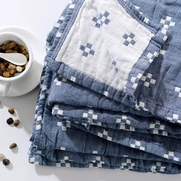Folded blue cotton gauze blanket with a corner turned back to show the cream reverse and the blue edge binding