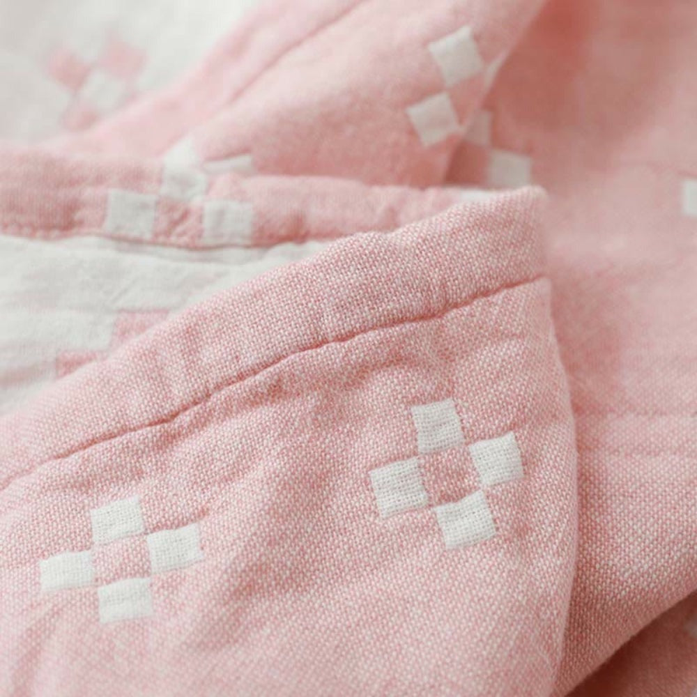 Close-up of the pink cotton gauze blanket folded over, white diamonds woven into the pink face
