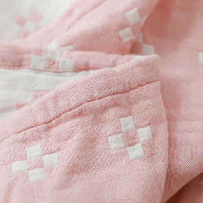 Close-up of the pink cotton gauze blanket folded over, white diamonds woven into the pink face