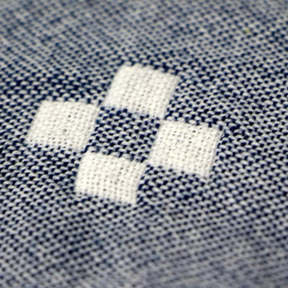 Macro of one woven diamond of four cream squares on the blue cotton weave