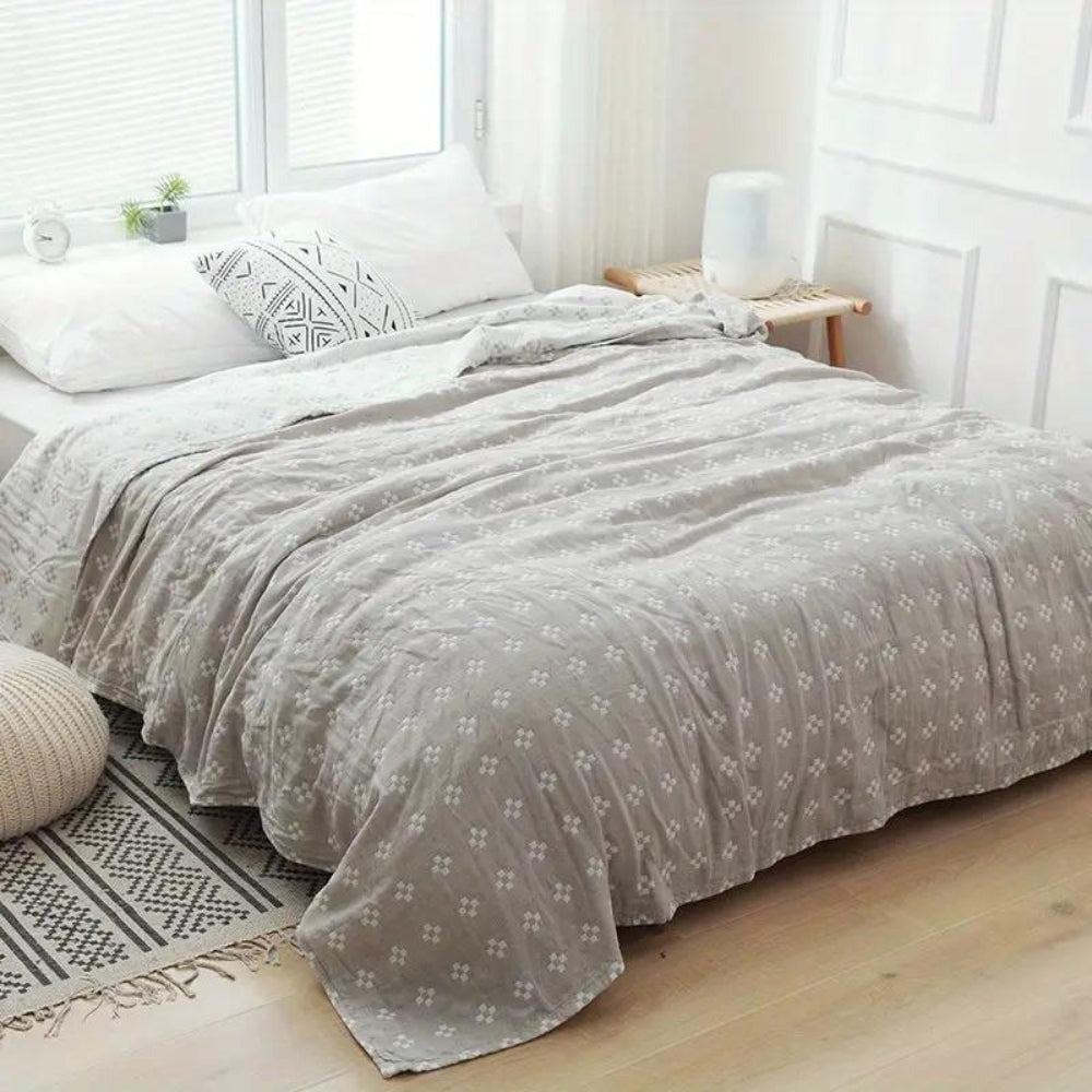 Gray diamond dot cotton blanket spread over a bed in a bright bedroom, white diamonds on soft gray