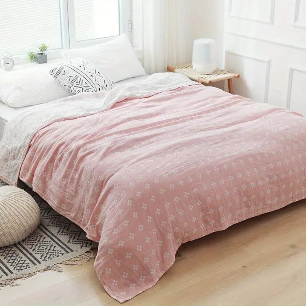 Pink diamond dot cotton blanket spread over a bed, white diamonds on dusty rose with the cream reverse at one corner