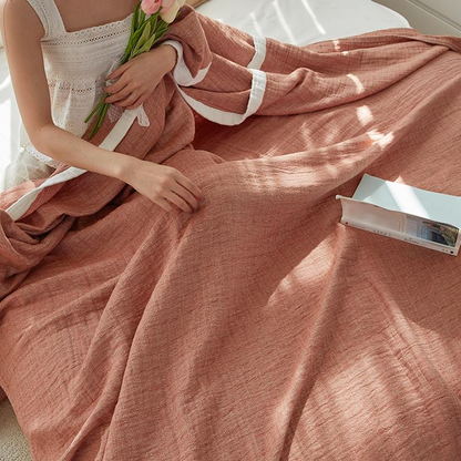 Muslin cotton blanket gathered over a woman's lap on a bed, the white edge band folded across it