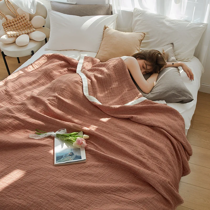 Woman asleep on a bed under a rust muslin cotton blanket with a white edge band