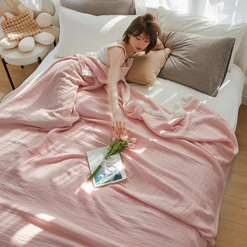 Woman lying on a bed under a pale pink muslin blanket, reaching for tulips on a book