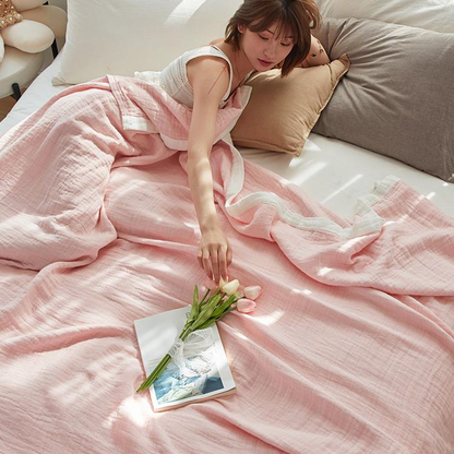 Pale pink muslin cotton blanket loosely spread over a bed, a woman resting against the pillows