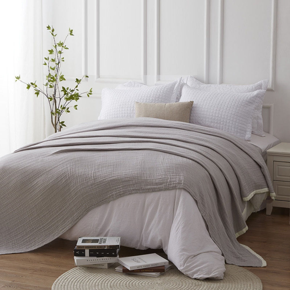 Gray muslin blanket draped across a made bed with white pillows in a white paneled bedroom