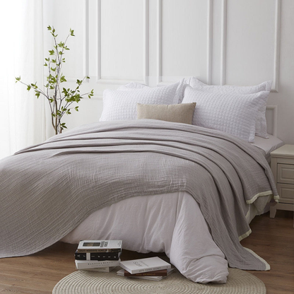 Gray muslin blanket draped across a made bed with white pillows in a white paneled bedroom