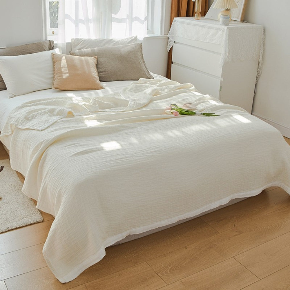 Cream muslin cotton blanket spread over a double bed, edged with a white band