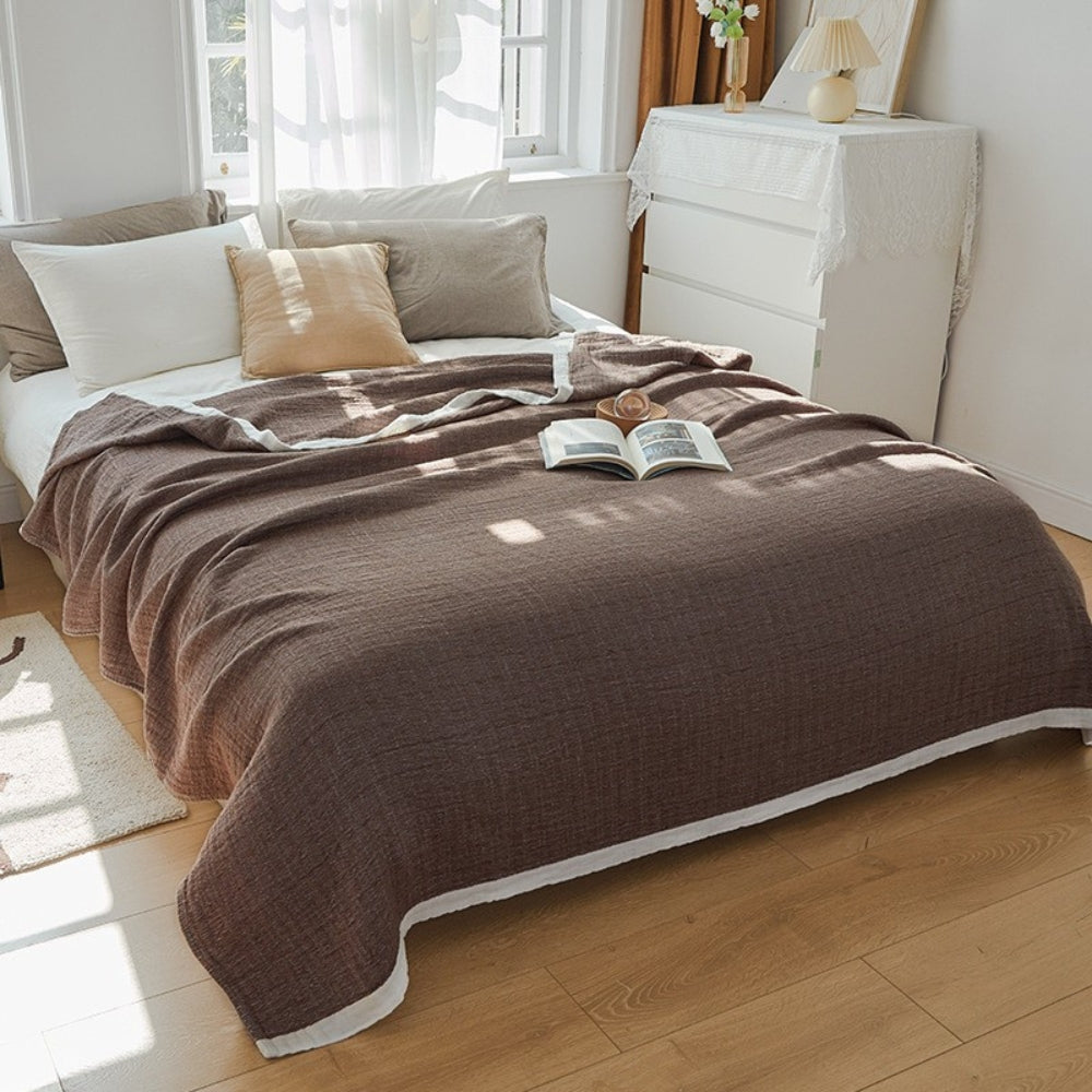 Deep brown muslin cotton blanket spread over a double bed, a white band along the hem
