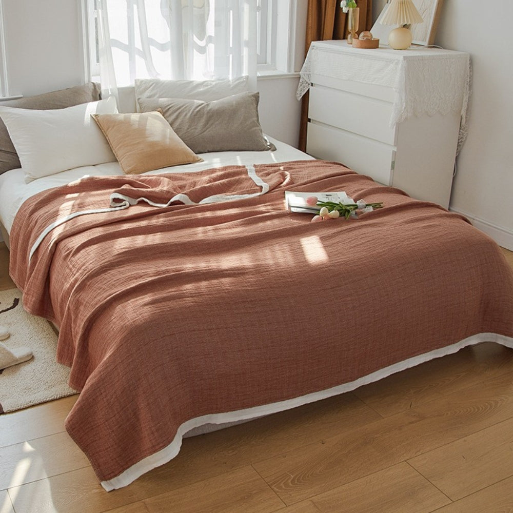 Rust muslin cotton blanket spread over a double bed, a white band along the hem