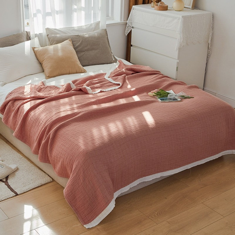 Coral muslin cotton blanket spread over a double bed, a white band along the hem