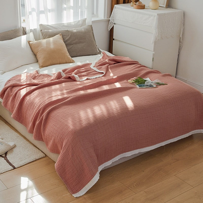 Coral muslin cotton blanket spread over a double bed, a white band along the hem