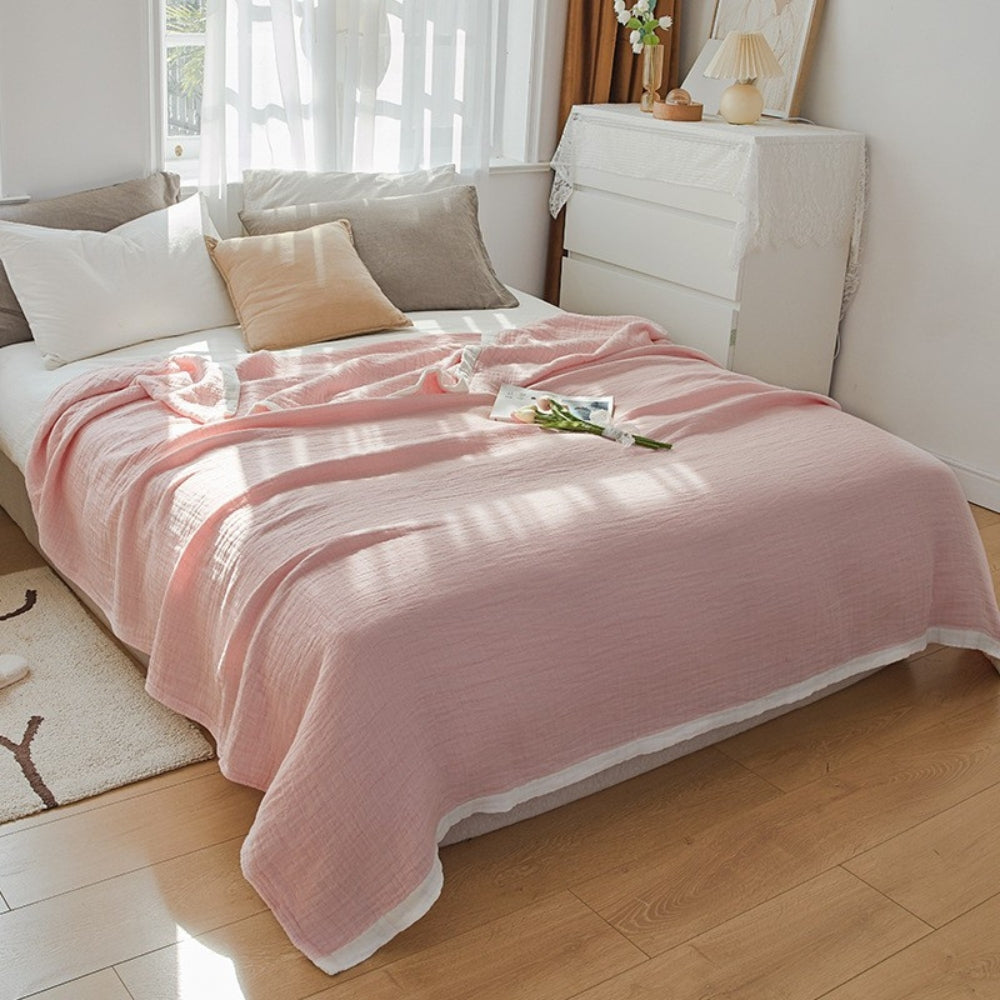 Pale pink muslin cotton blanket spread over a double bed, a white band along the hem