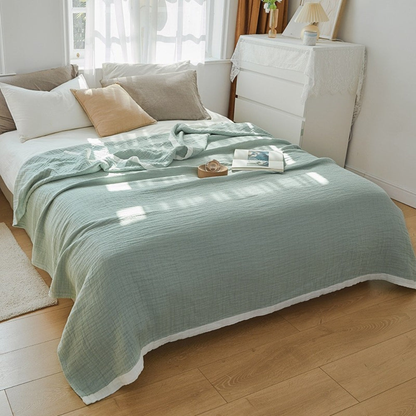 Sage green muslin cotton blanket spread over a double bed, a white band along the hem