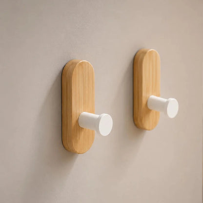 Close view of two light wood wall hooks with matte white pegs on a gray wall