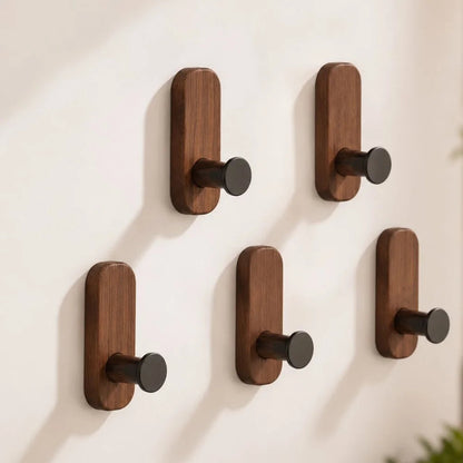 Five walnut wall hooks with black pegs on a white wall, two above three