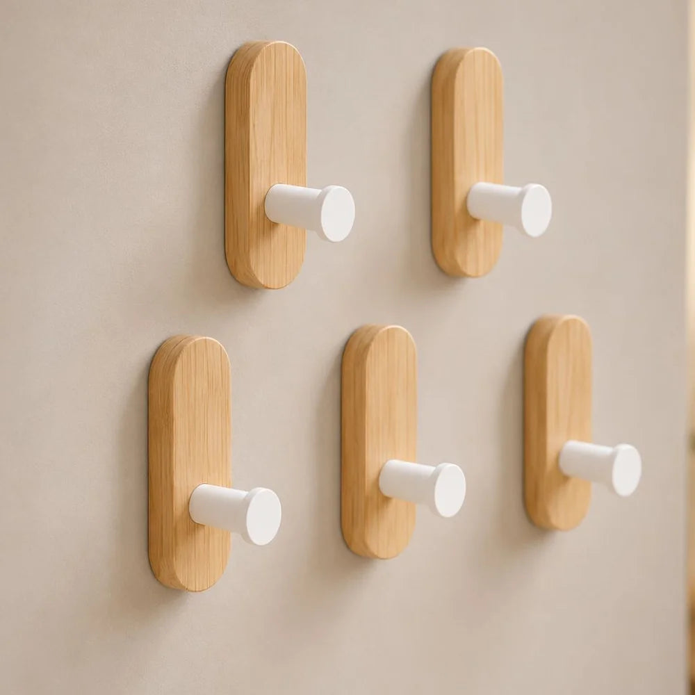 Five light wood wall hooks with white pegs on a light gray wall, two above three