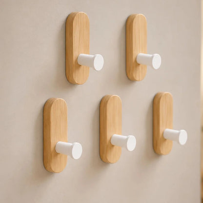 Five light wood wall hooks with white pegs on a light gray wall, two above three