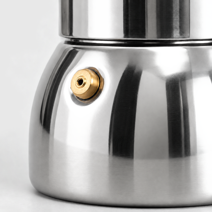 Close-up of the brass safety valve on the polished stainless steel base of a moka pot