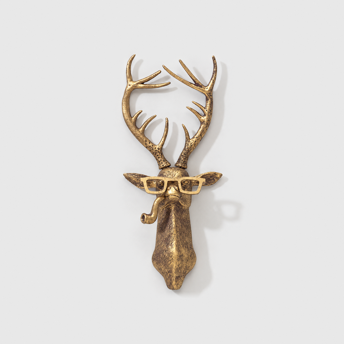 Deer head wall sculpture in antique gold-tone resin, with rectangular glasses and a pipe, on a plain light gray wall