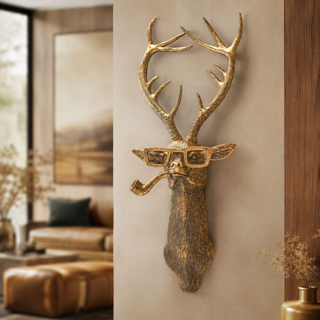 Gold-tone deer head sculpture with glasses and a pipe hung on a beige wall in a living room with a leather sofa