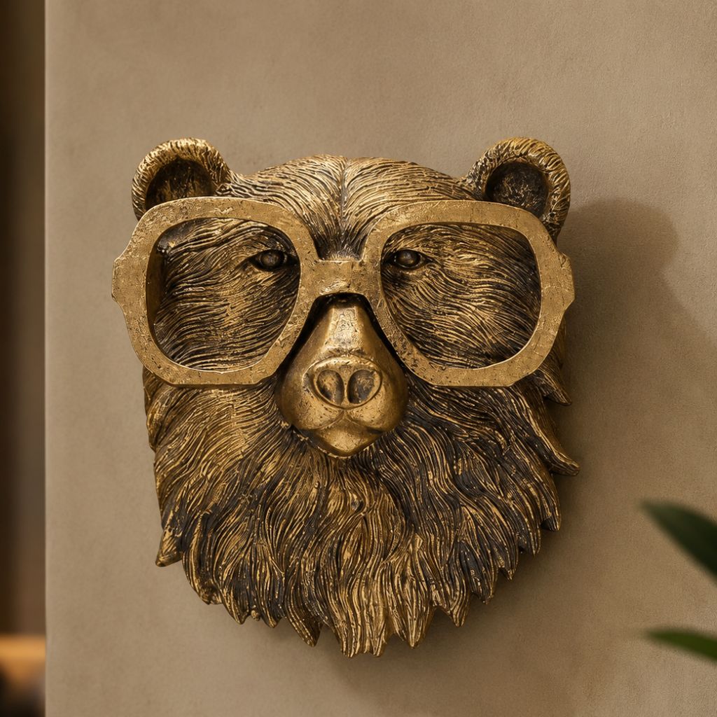 Gold-tone bear head sculpture wearing big rounded glasses on a beige wall