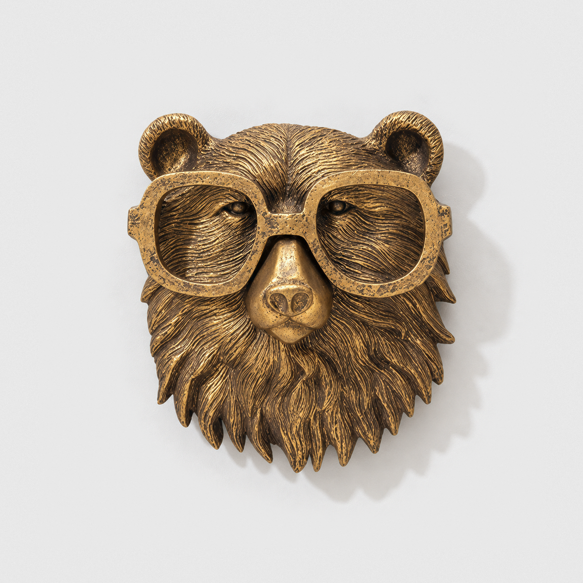 Bear head wall sculpture in antique gold-tone resin, with oversized rounded glasses, on a plain light gray wall