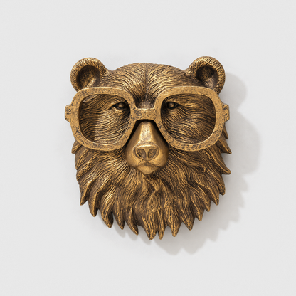 Bear head wall sculpture in antique gold-tone resin, with oversized rounded glasses, on a plain light gray wall