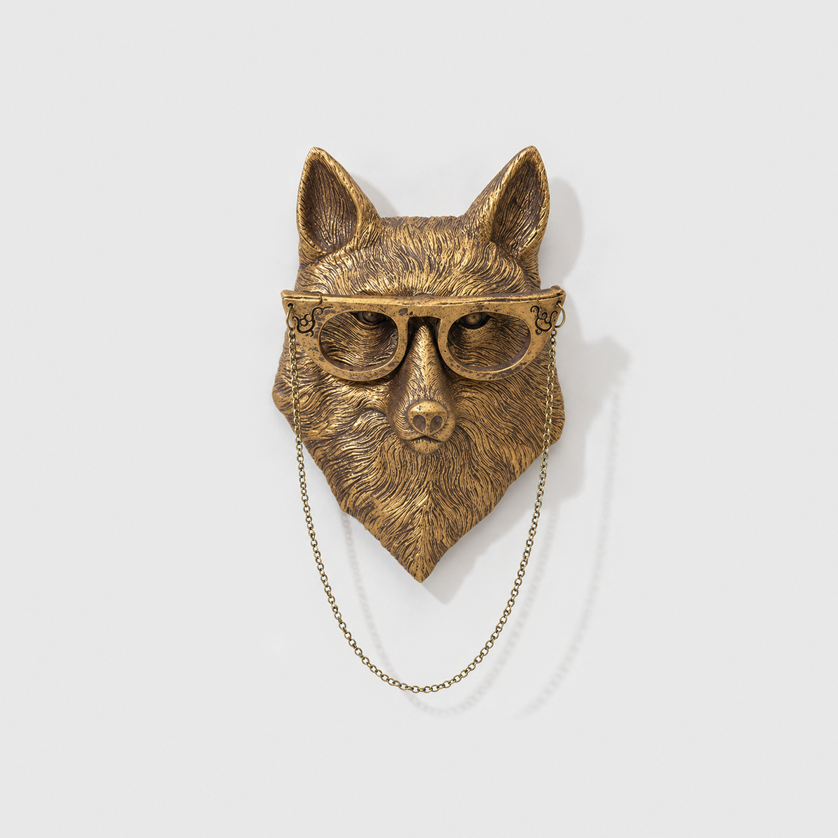 Fox head wall sculpture in antique gold-tone resin, with glasses and a fine chain, on a plain light gray wall
