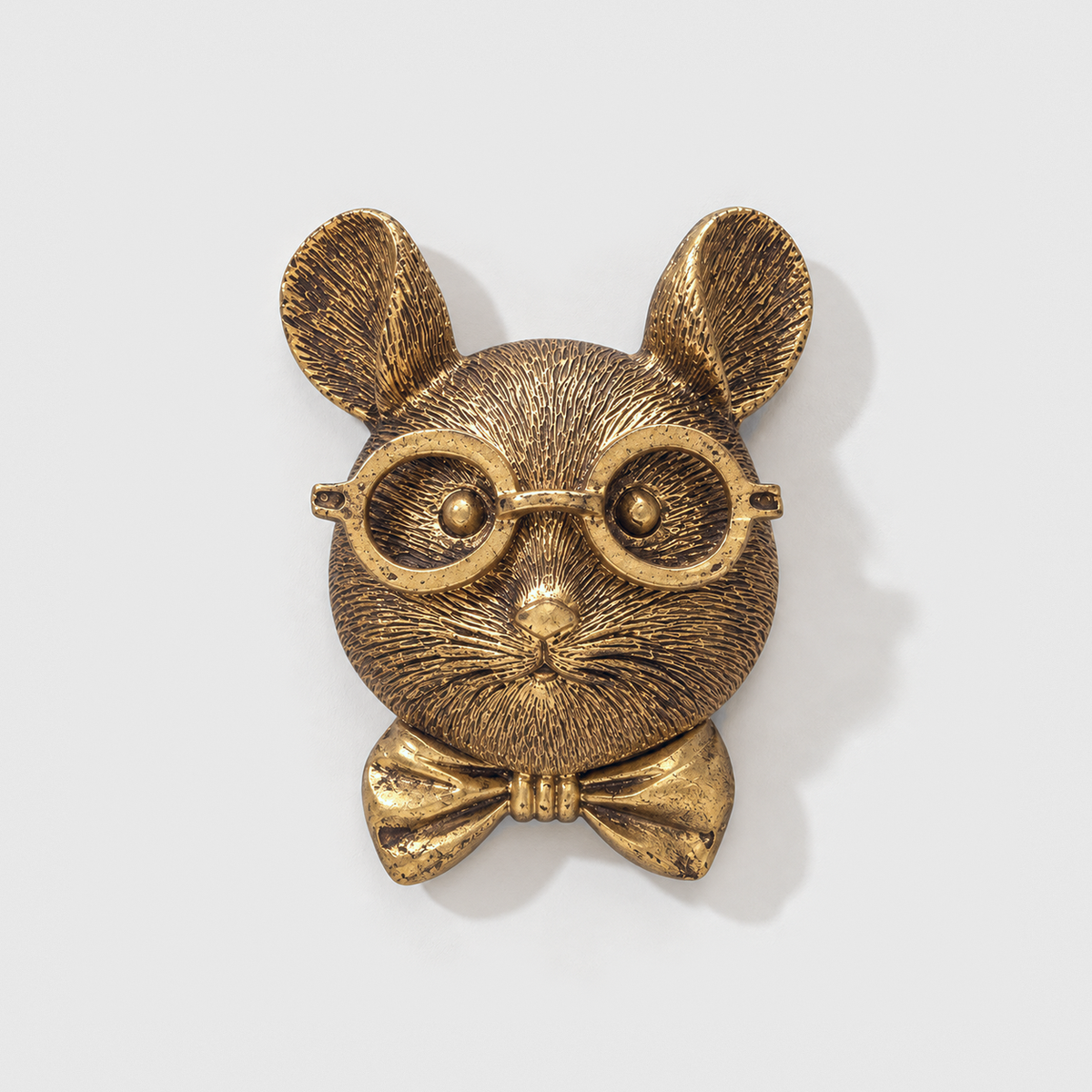 Mouse head wall sculpture in antique gold-tone resin, with round glasses and a bow tie, on a plain light gray wall
