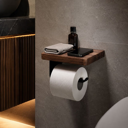 Walnut toilet paper holder with shelf on a gray stone tile wall, a phone, a folded hand towel and an amber bottle on the shelf above the roll