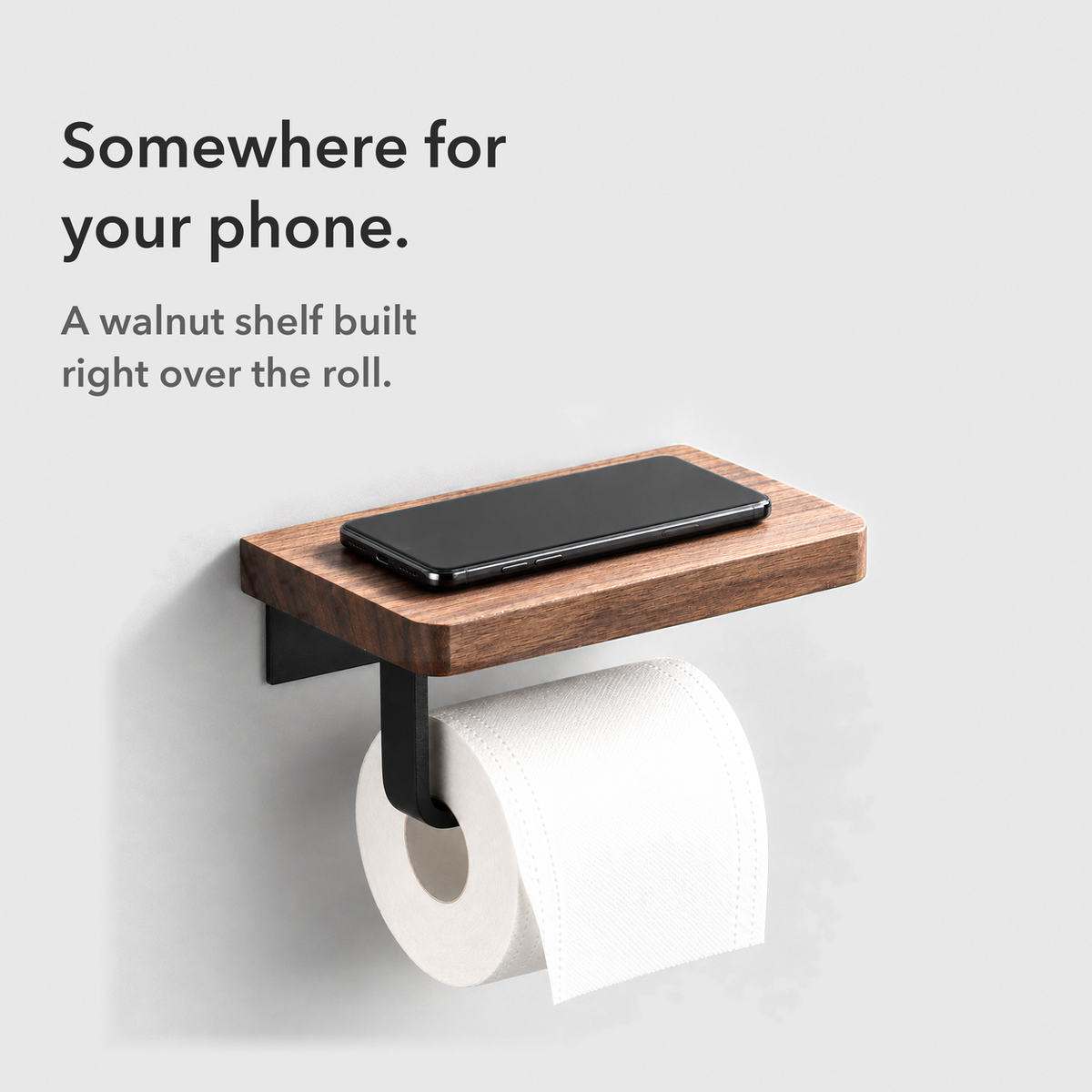 Card reading Somewhere for your phone: a phone lying on the walnut shelf of the toilet paper holder above the roll
