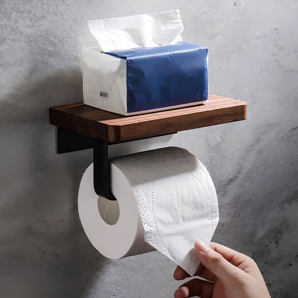 Pack of tissues on the walnut shelf of the toilet paper holder while a hand pulls a sheet from the roll