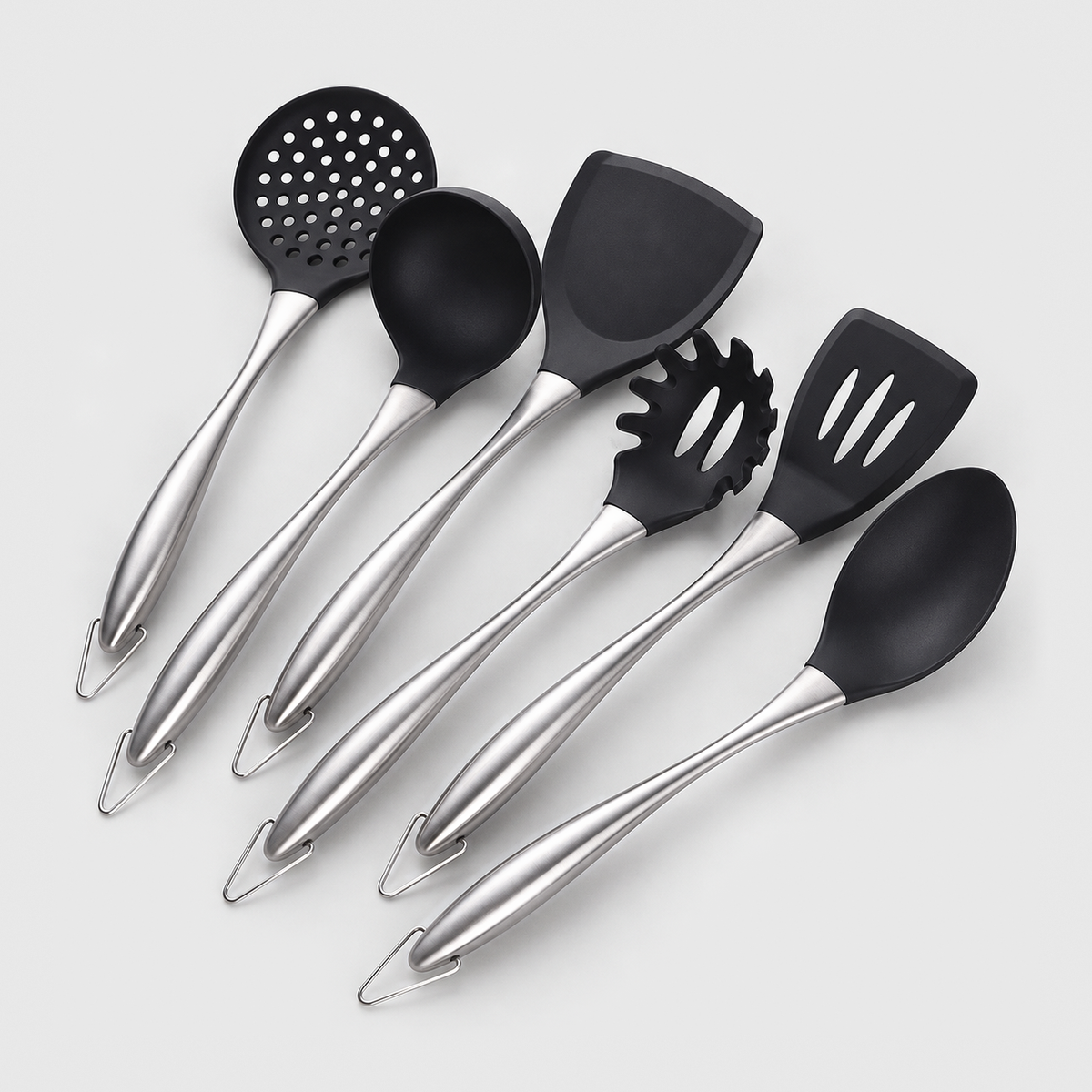 Six-piece cooking utensil set with black non-stick heads and brushed silver stainless steel handles, laid out on a light gray background
