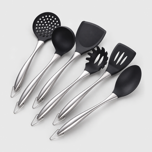 Six-piece cooking utensil set with black non-stick heads and brushed silver stainless steel handles, laid out on a light gray background