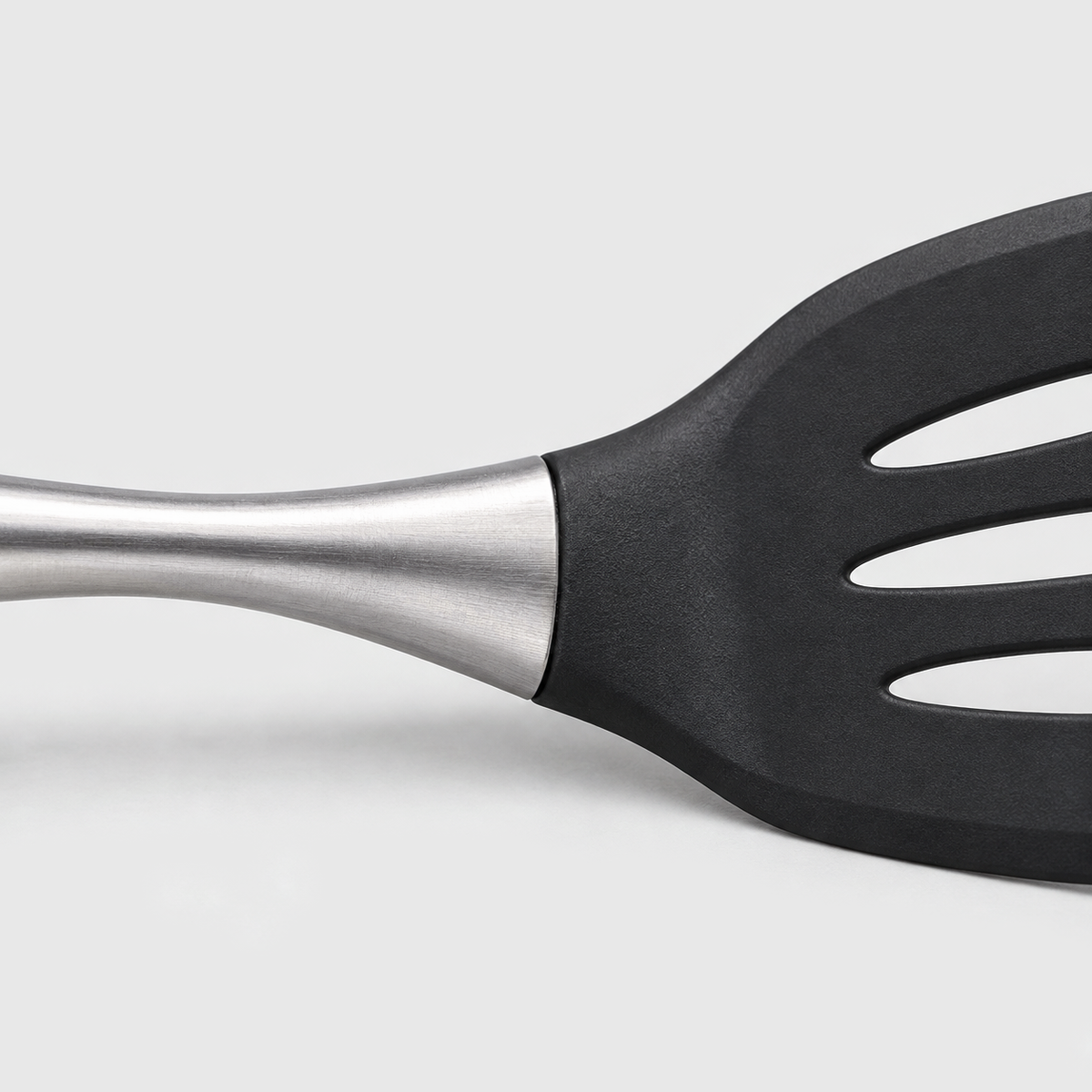 Close-up of a brushed stainless steel handle meeting the black head of a slotted turner