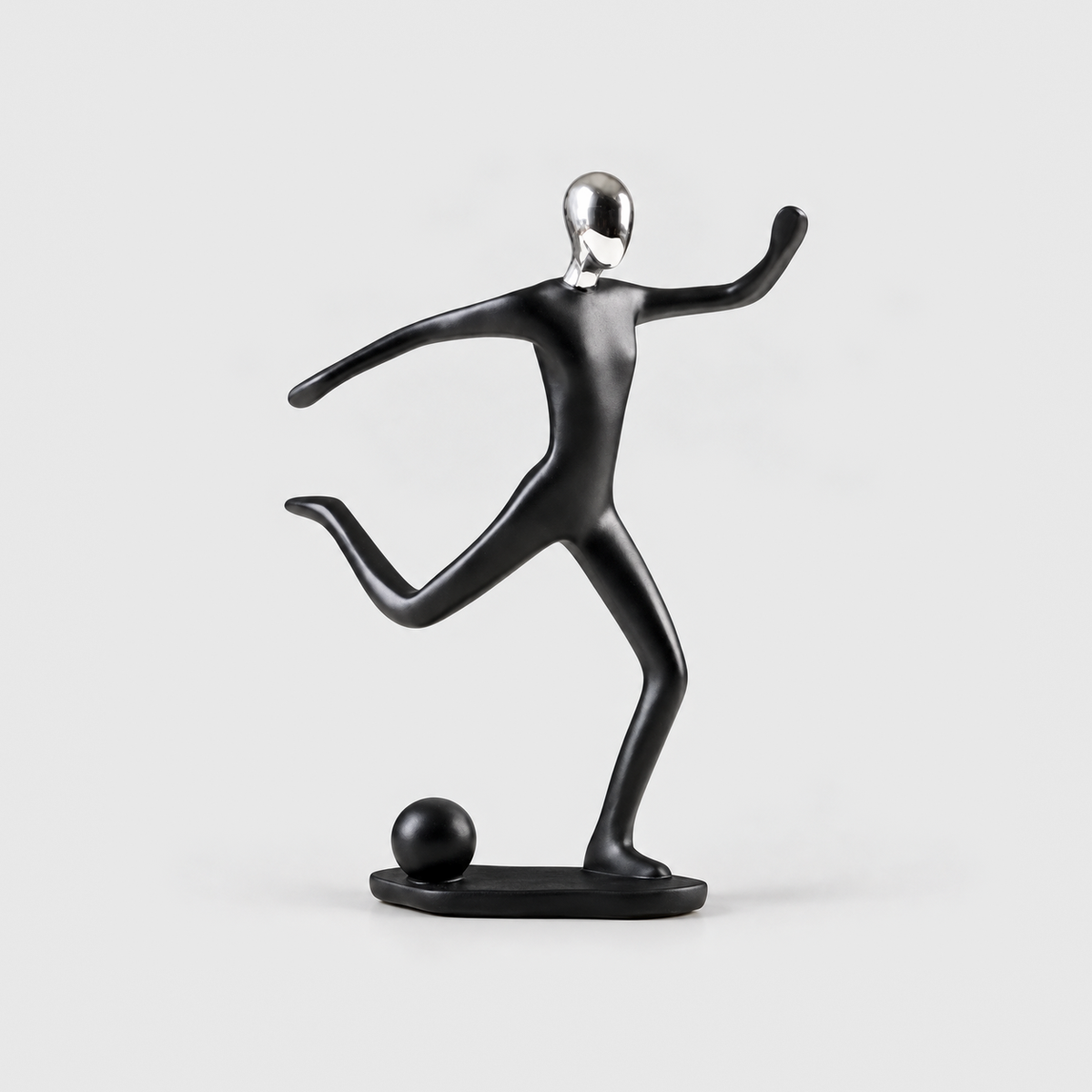 A matte black soccer player sculpture mid-kick with a ball on the base, on a light gray background