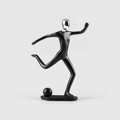 A matte black soccer player sculpture mid-kick with a ball on the base, on a light gray background