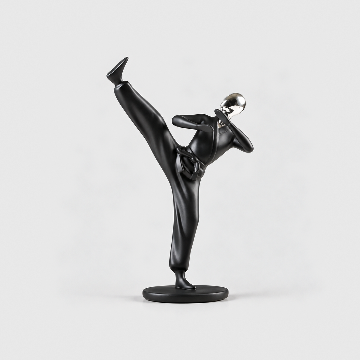 A matte black kung fu sculpture holding a high kick on one leg, on a light gray background