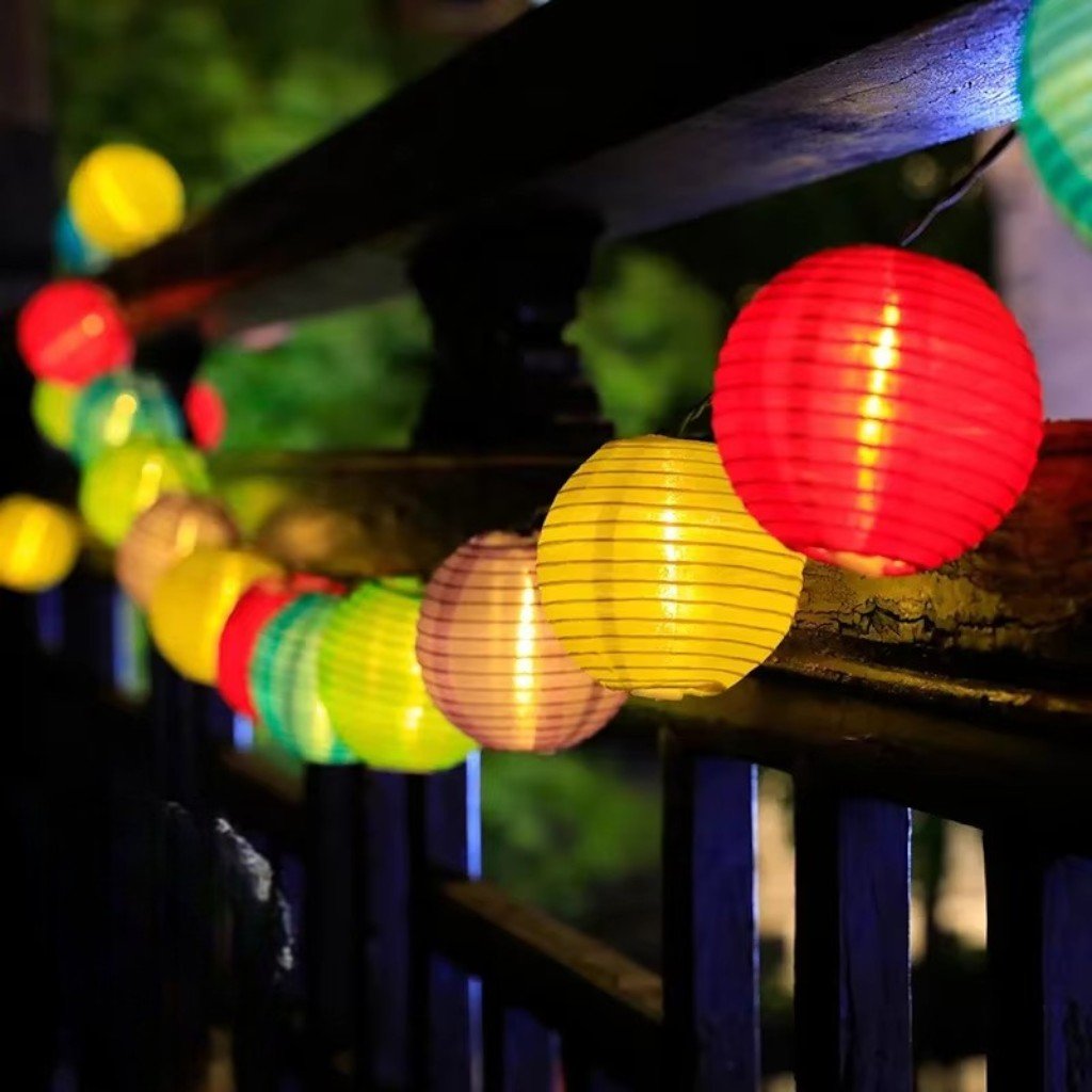 Close-up of red, yellow and green fabric lanterns lit along a deck railing at night