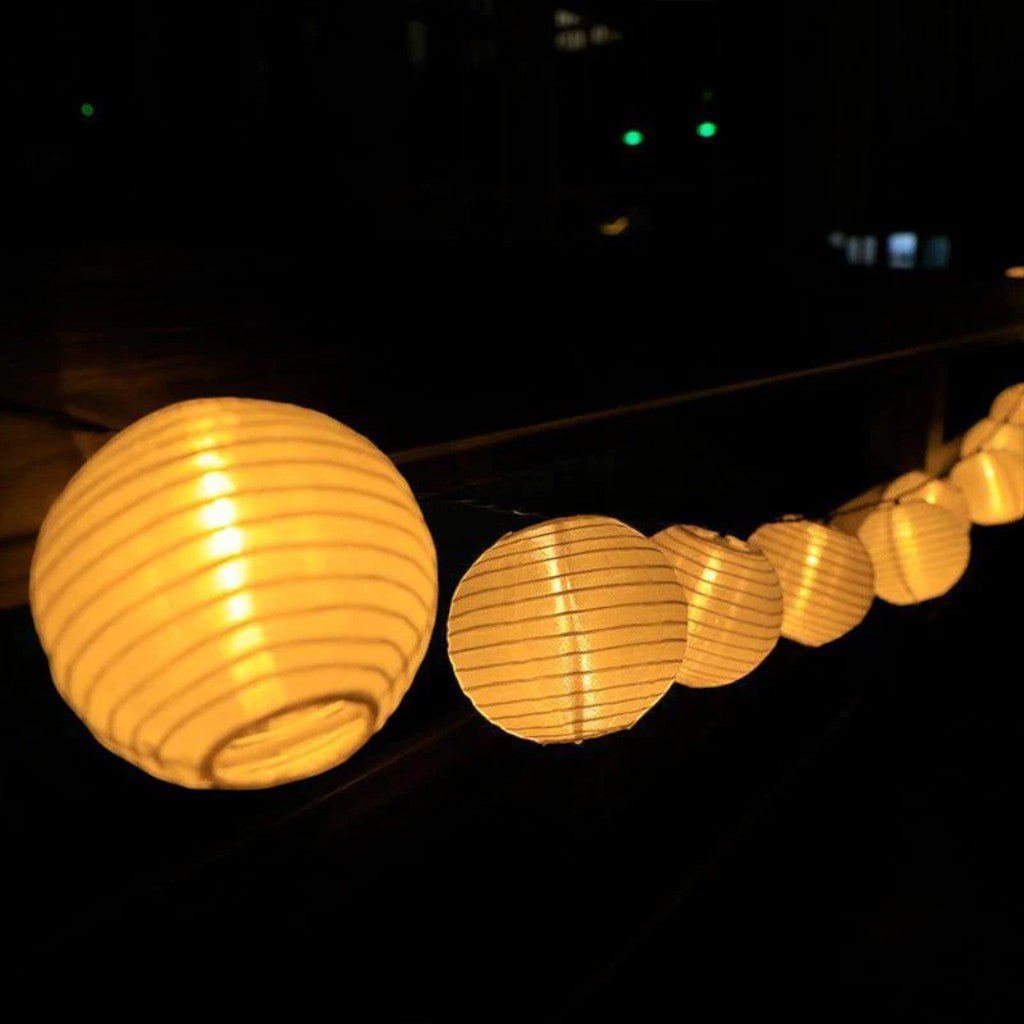 Close-up of white fabric lanterns glowing warm gold at night, showing the ribbed fabric